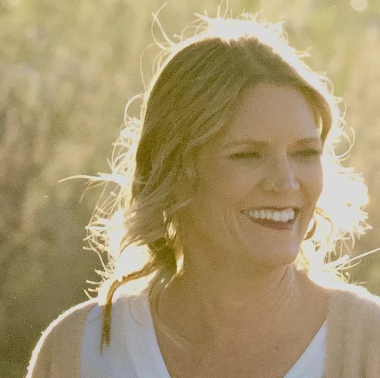 A woman smiling for the camera in front of trees.